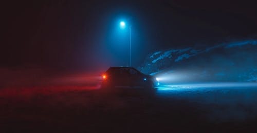 En bil med tændte forlygter står på en grusvej i mørket.