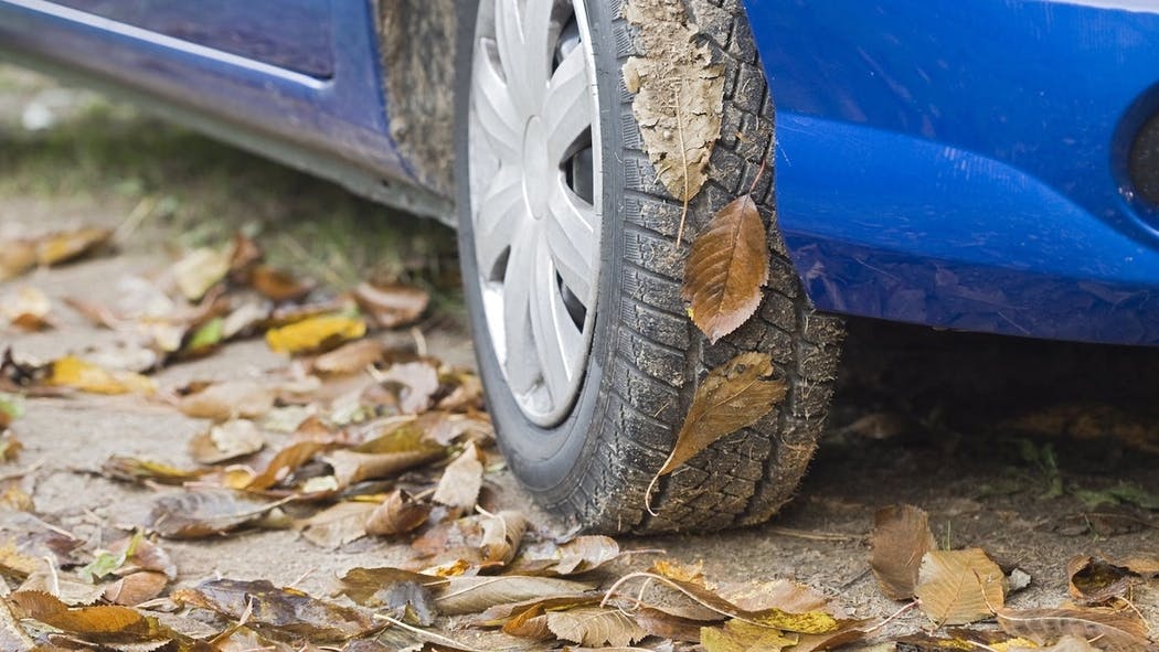  Nærbillede af hjulet i en blå bil parkeret på en vej fyldt med efterårsblade.