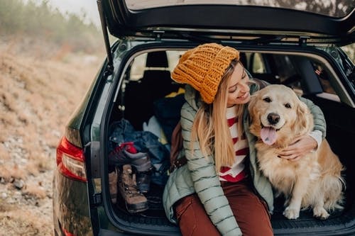  Smilende kvinde sidder på bagsædet af en bil med en hund ved siden af ​​sig.